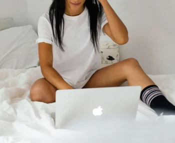 Une jeune femme assise sur son lit avec son laptop